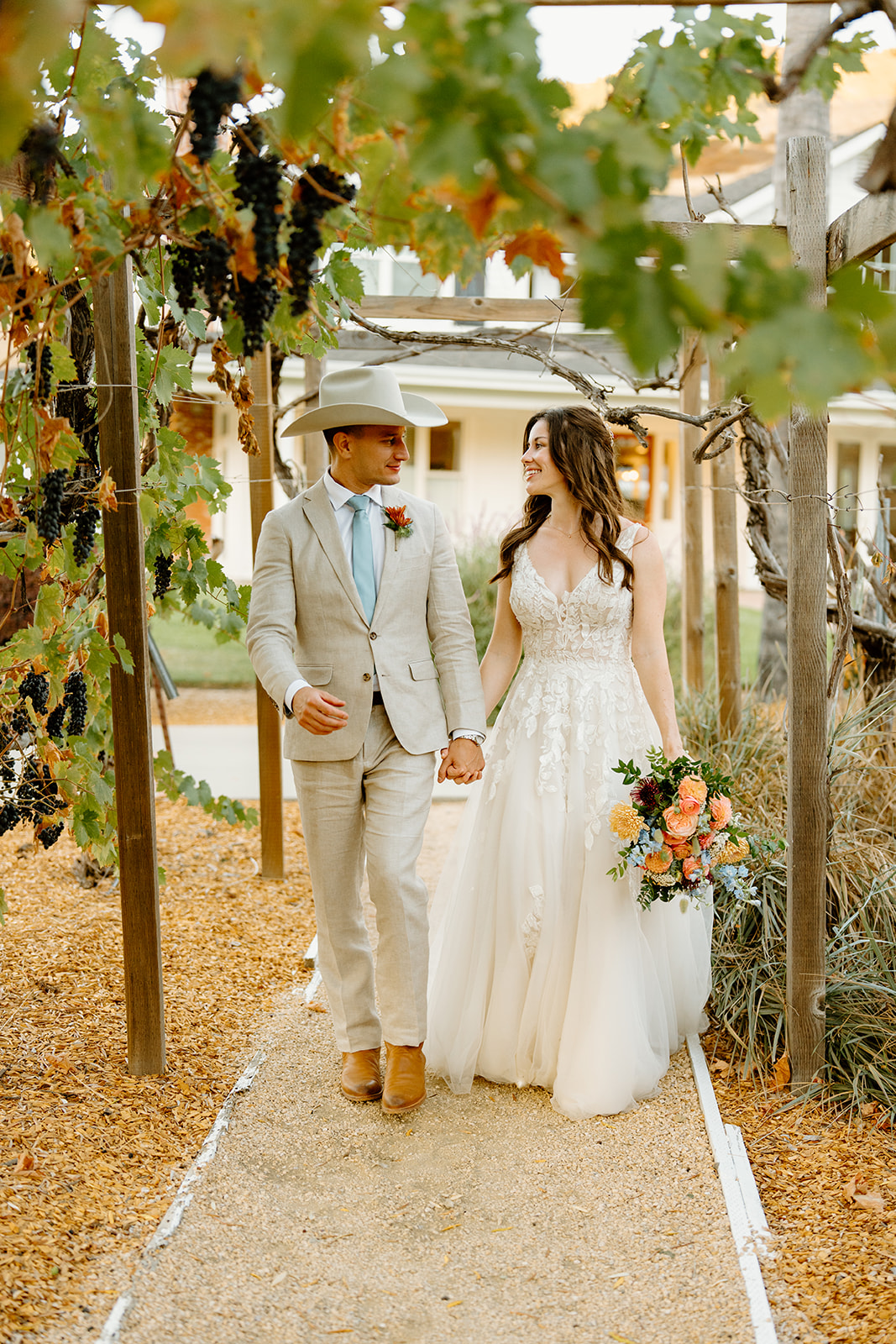 bride and groom with hat walk vineyard at Higuera Ranch, San Luis Obispo CA, photography by Cobblestone