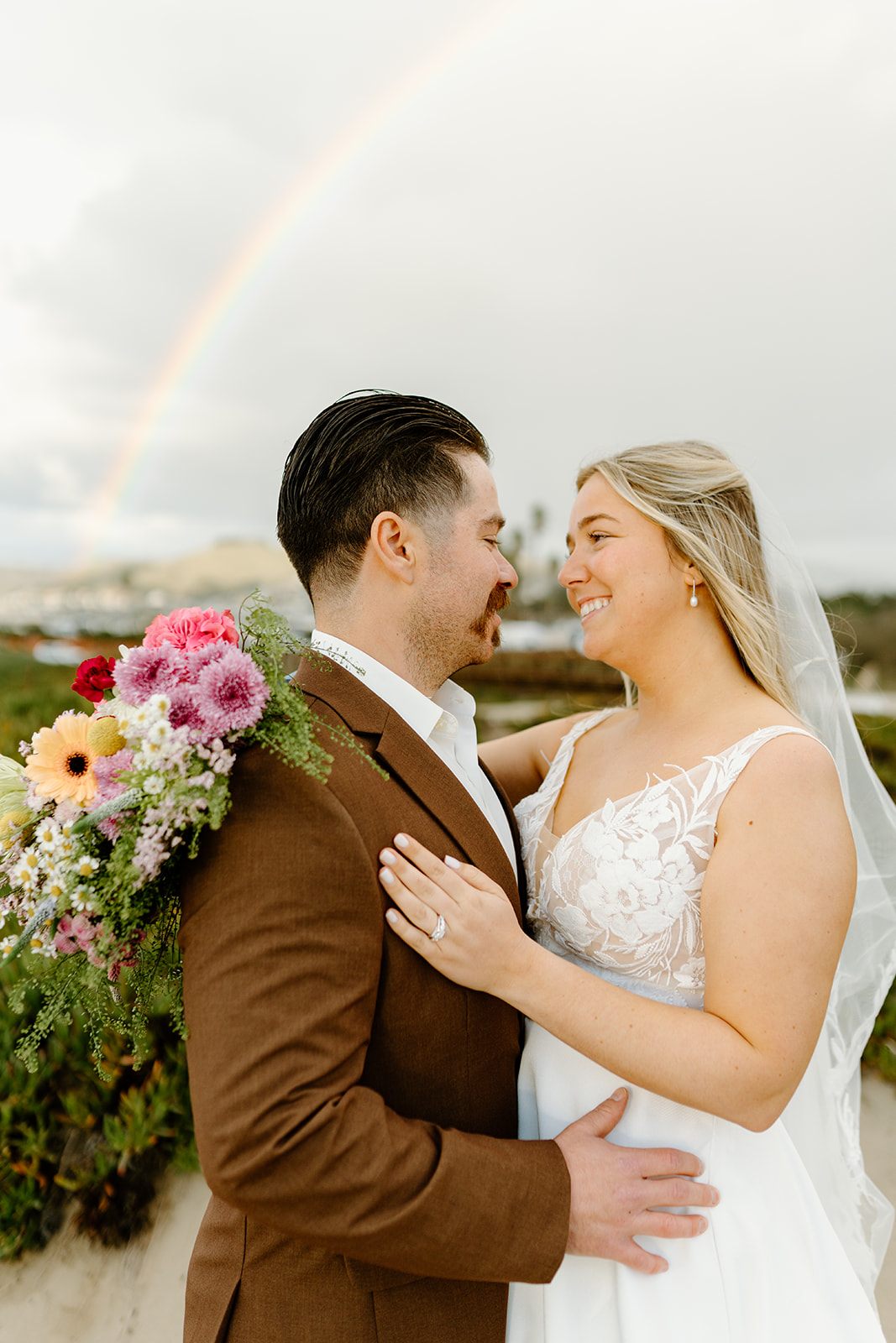 Senteno & Katie holding each other under rainbow with flowers. cobblestone weddings photography